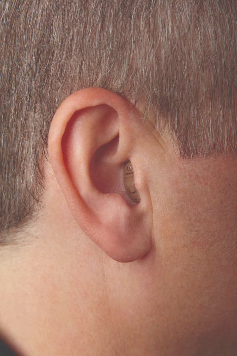 Close-up of a person's ear with a small CIC hearing aid just visible at the canal opening