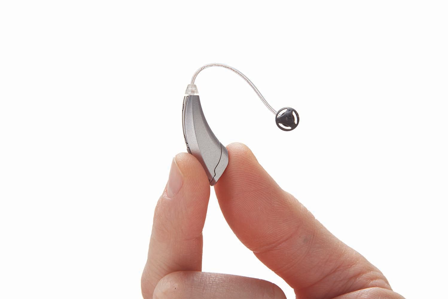 Hand holding a small silver behind-the-ear hearing aid