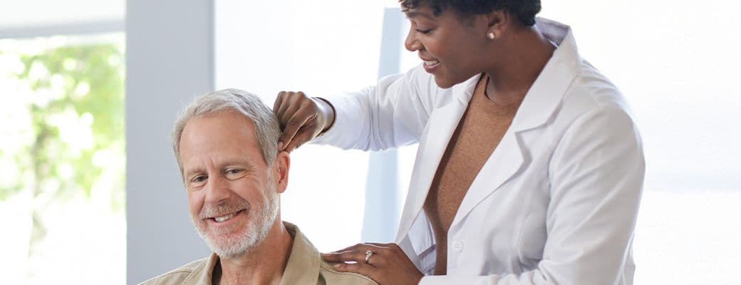 Hearing care professional fitting a hearing aid behind the ear of a smiling older man