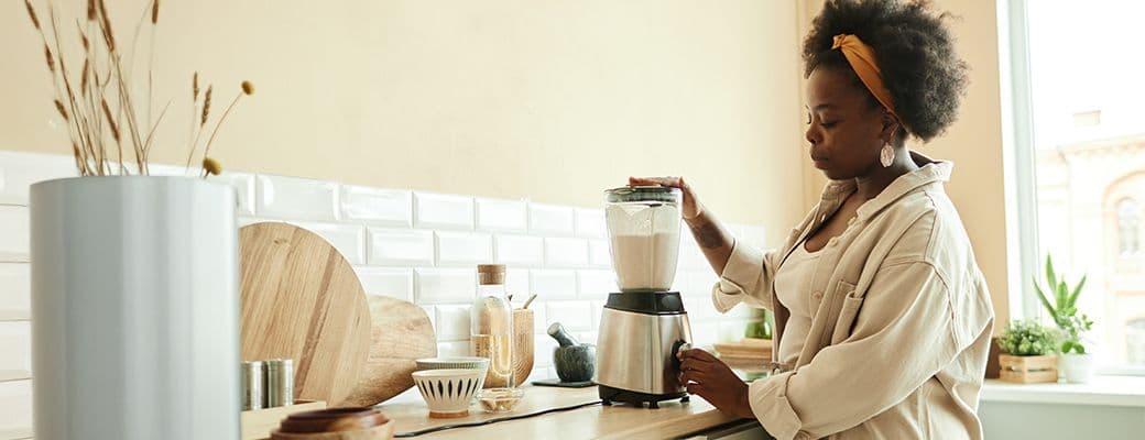 Woman using a countertop blender in a bright kitchen