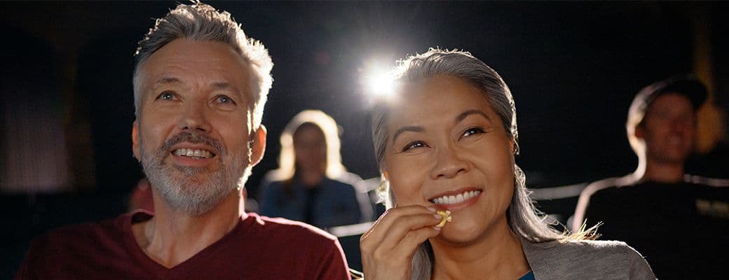 Older couple smiling in a darkened cinema while sharing a bag of popcorn