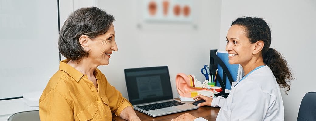Hearing care professional reviewing results with an older patient at a desk with an anatomical model of the ear